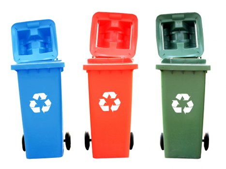 Three wheeled rubbish bins positioned side by side outdoors, representing recycling and waste disposal options commonly used in residential or commercial waste management. The bin on the left is blue with a closed lid, made of plastic with a smooth textured finish and a white recycling symbol on its front. The middle bin is red, also made of plastic with a smooth surface, featuring a hinged lid that is partially open, revealing the empty interior. The bin on the right is green, similarly plastic with a matte finish, and its lid is slightly ajar, showing an open compartment. Each bin has black rubber wheels attached at the sides at the base for mobility. The background is plain and neutral, with no additional environmental details, emphasizing the bins’ shapes, colors, and functional design as part of waste removal services, such as those provided by Business Waste Removal Stratford in the local Stratford area of London postcode E20.